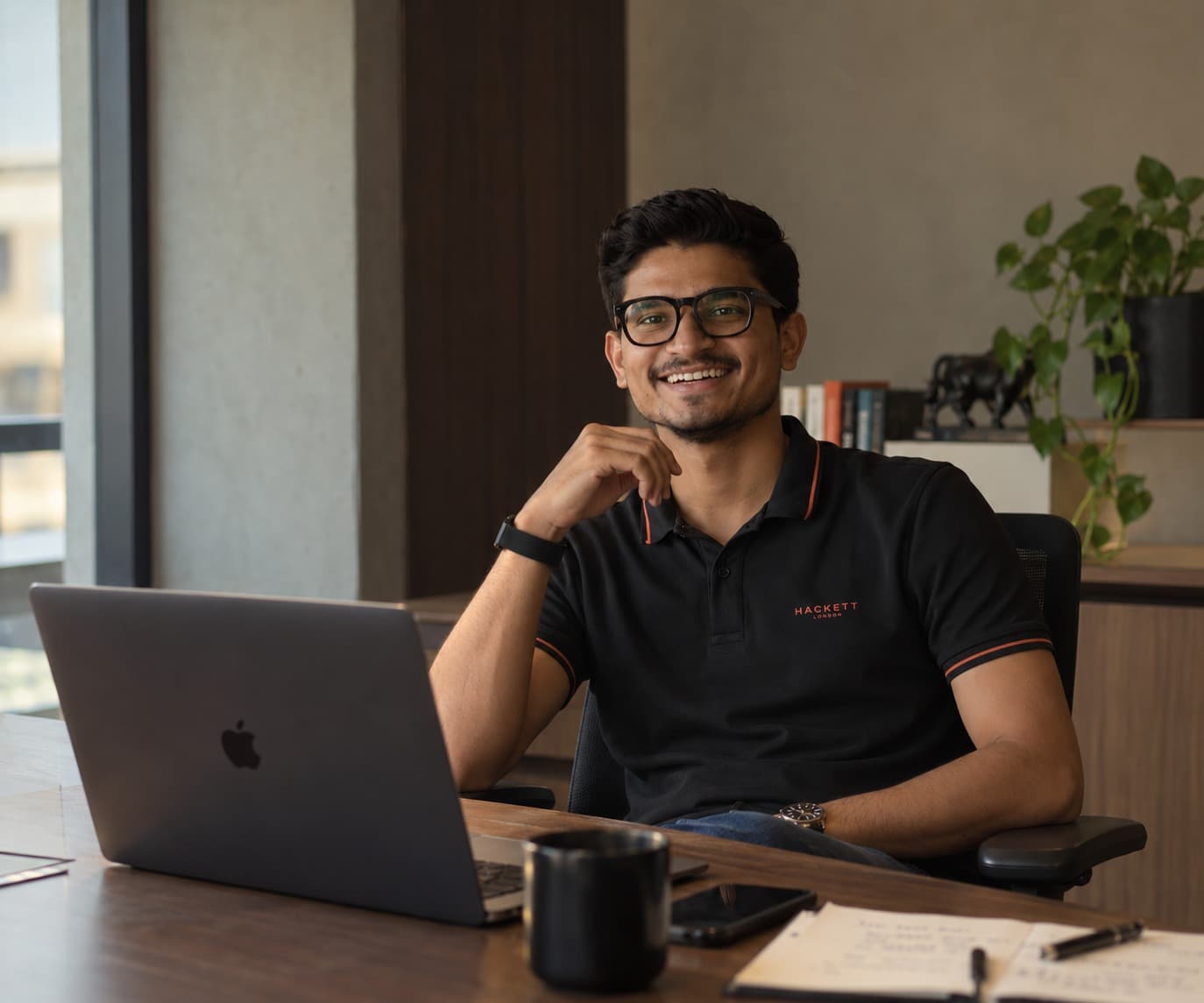 Ramsingh Vaghelaa smiling at his desk with a laptop and notebook